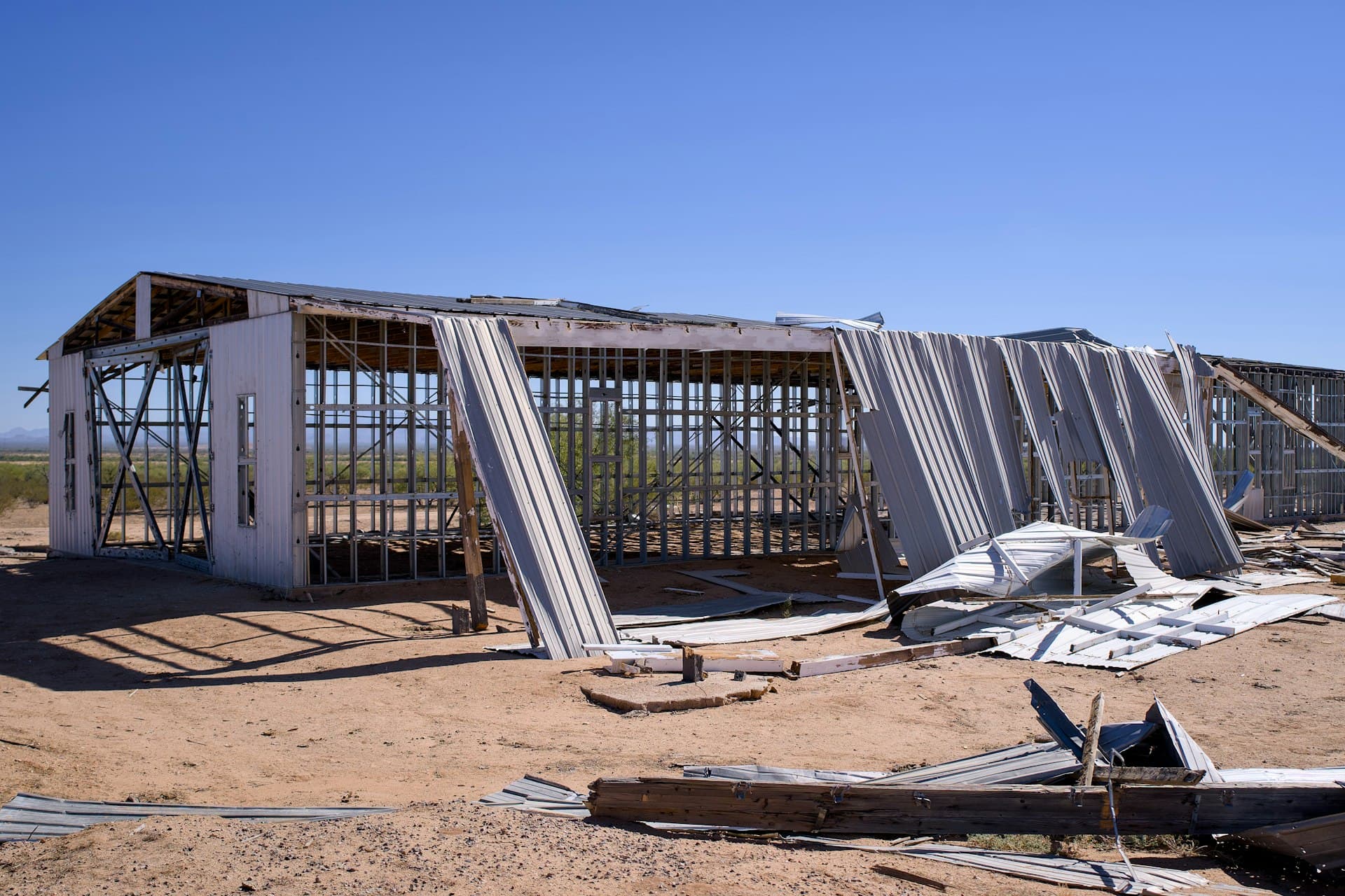 Wind-damaged commercial building with exposed framing and torn metal roofing